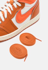 Nike-sneakers med orange läder och vit textil, med en strukturerad yta, orange accenter och två rullade orange snören.