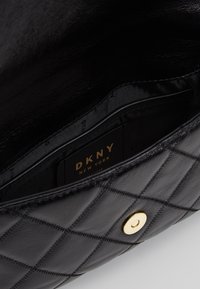 Černá prošívaná kožená taška s vnitřní částí se zlatým kováním a štítkem DKNY. Hladká textura a minimalistický design s tmavým podšívkou.