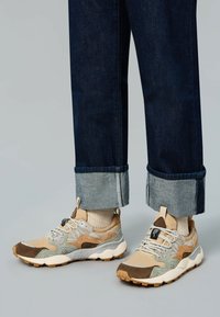 Zapatillas con una combinación de materiales en beige, marrón y gris; superposiciones texturizadas; cordones blancos; suelas de goma; y soporte acolchado en el tobillo.