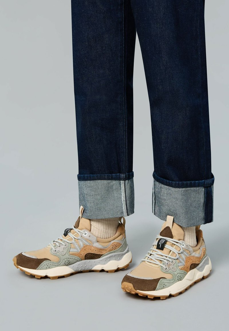 Zapatillas con una combinación de materiales en beige, marrón y gris; superposiciones texturizadas; cordones blancos; suelas de goma; y soporte acolchado en el tobillo.