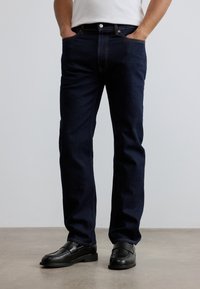 Σκούρο μπλε τζιν με ευθεία γραμμή, διαθέτει εμπρόσθιες τσέπες, διακριτικές ραφές και κλασικό κούμπωμα με κουμπί. Συνδυάζεται με μαύρα μοκασίνια.