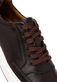 Brązowe skórzane sneakersy z zaokrąglonym noskiem, kontrastową białą podeszwą i ciemnobrązowymi sznurówkami. Charakteryzują się gładką teksturą i minimalistycznym designem.