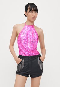 Haut à paillettes roses en halter, au design ajusté, associé à un short noir avec des franges perlées le long des poches.