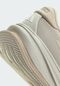 Beige sportieve schoen met een gestructureerde mesh bovenkant en een gladde rubberen zool. Bevat een gevoerde hiel en subtiele branding op de zijkant.