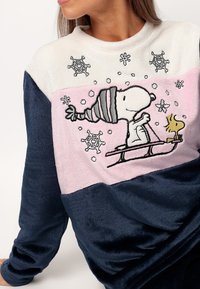 Sudadera de forro polar con parte superior crema, centro rosa con una ilustración de dibujos animados de Snoopy y mangas azul marino; textura suave con detalles de copos de nieve.