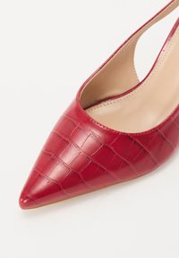 Rød spiss pumps laget av teksturert lær med et krokodillemønster; har en beige innside og en slank silhuett.