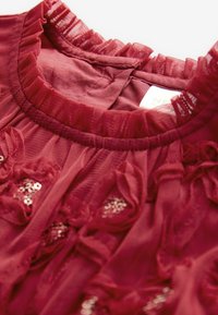 Burgundy klänning med volangkrage, blommiga detaljer och paljetter på genomskinlig tyg. Slät innerfoder.