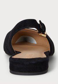 Musta mokkanahka sandaali avonaisella varpaalla ja takana, jossa on kapea nilkkahihna ja tasapohja. Sisäpuolella on sileä beige vuori.