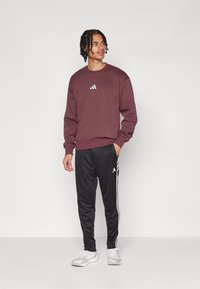 Bordeaux sweatshirt met een ronde hals en wit logo op de borst, gecombineerd met zwarte sweatpants met witte zijstrepen en logo.