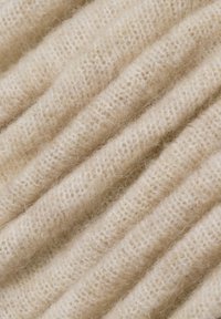 Lichtbeige gebreide stof met een geribbelde textuur, die fijne vezels en een zachte dikte vertoont, gerangschikt in parallelle plooien.