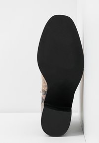 Svart gummisula med texturerad yta och mönstrad övre i beige och bruna nyanser. Rund tåform och hög ankel-design.