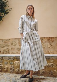 Chemise en coton rayée avec un devant à boutons, associée à une jupe assortie. Tissu léger, coupe décontractée, avec poches et ballerines noires.