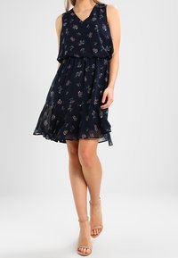 Navyfarbendes Blumenkleid aus leichtem Material, mit V-Ausschnitt, ärmellosem Design, geschichteter Rock und zarten Blumenmustern.