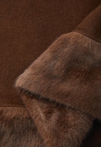 Hnědá vlna a kožešinová tkanina vrstvená s viditelnou detailní texturou v pohledu zblízka.