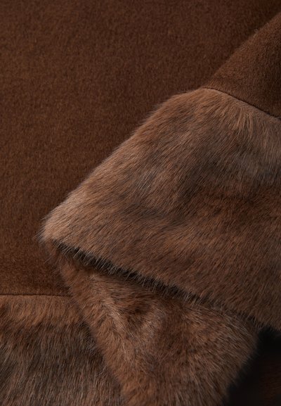 Tessuto di lana e pelliccia marrone stratificato con texture dettagliate visibili in primo piano.