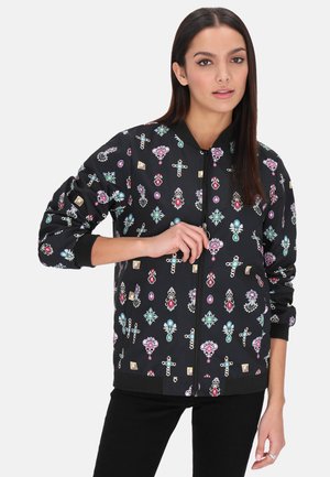 Giacca bomber nera con un vivace motivo floreale e di gioielli. Manicotti e vita a coste, con chiusura frontale a cerniera. Materiale leggero.
