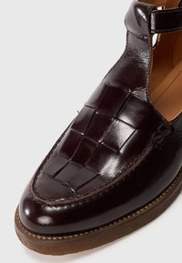 Dark brown leather shoe with woven upper design. Rounded toe and stitched detailing. Flat rubber sole with slight texture for grip.