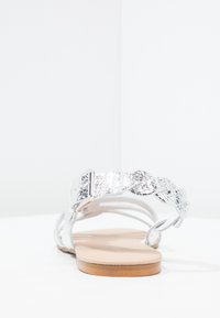 Hopeat litteät sandaalit punottuine remmeineen, metallic-finishilla ja yksinkertaisella soljella. Vaaleanruskea sisäpohja ja minimalistinen muotoilu.