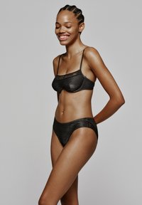 Zwart lingerieset met een bralette met dunne bandjes en een bijpassende high-waisted slip, beide in een textuurstof met kanten accenten.