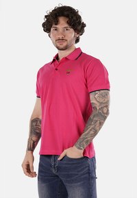Polo shirt rosa con colletto, maniche corte e dettagli blu navy. Presenta un piccolo logo ricamato sul petto. Tessuto morbido.