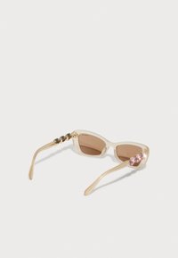 Óculos de sol com armação transparente bege, lentes castanhas, acabamentos em tom dourado e três detalhes rosa na haste; detalhes em corrente texturizada.