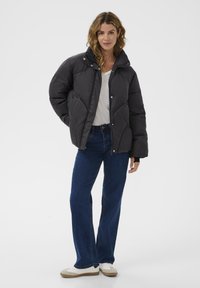 Černá péřová bunda s vysokým límcem, prošívaný design, přední zapínání na patentky, v kombinaci s modrými rovnými džíny a bílými teniskami.