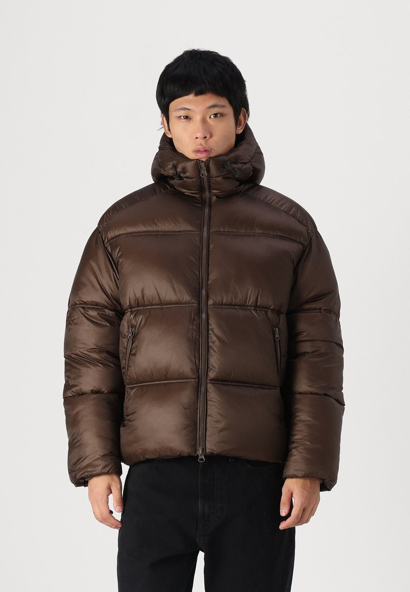 Chaqueta de plumas marrón con cuello alto, cierre de cremallera y paneles cosidos. Tiene una textura suave y un bolsillo lateral.