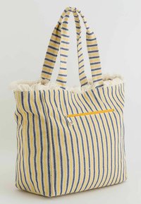 Sac fourre-tout rayé avec des rayures jaunes et bleu marine, en tissu texturé, bords duveteux, et une poche zippée à l'avant. Poignées à plusieurs brins.