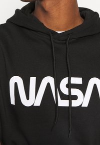 Schwarze Kapuzenjacke aus Baumwolle mit einer Kordelzugkapuze und einem weißen, gedruckten "NASA"-Logo auf der Brust.