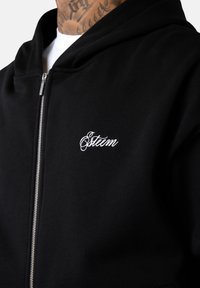 Haut à capuche zippé noir en mélange de coton, avec un logo brodé blanc "Esteem" sur la poitrine gauche et un tissu doux et texturé.