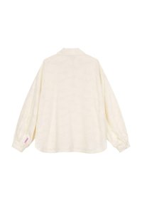 Camicia oversize a maniche lunghe di colore crema chiaro con una texture morbida, polsini abbottonati e un motivo sottile. Presenta un colletto a punta e un'etichetta laterale.
