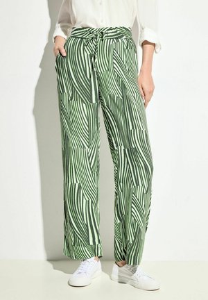Pantalones de pierna ancha con un estampado verde y blanco, con cintura ajustable por cordón, que presentan un acabado texturizado y bolsillos laterales. Combinados con zapatillas blancas.