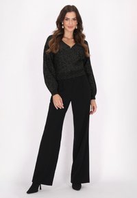 Pullover nero scintillante con scollo a V e maniche a palloncino, abbinato a pantaloni a gamba larga neri a vita alta e tacchi a punta.
