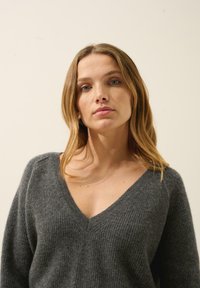 Szary sweter z dzianiny z dekoltem w kształcie litery V, żebrowaną strukturą i luźnym krojem. Materiał wydaje się miękki i wygodny.