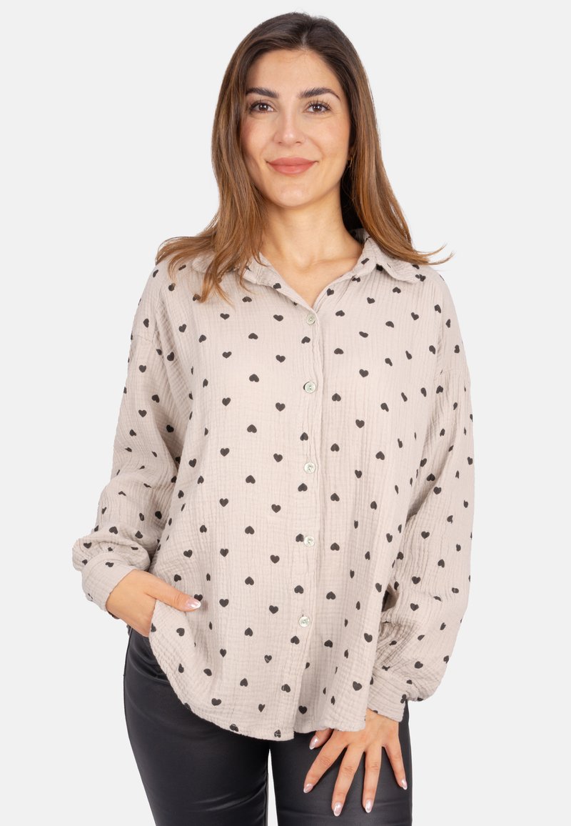 Light beige button-up shirt with black heart patterns, made of textured fabric. Features a collar and long sleeves, with a relaxed fit.