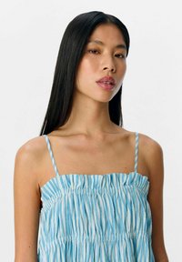 Robe sans bretelles, bleu clair avec des rayures verticales blanches, présentant une texture froncée et de fines bretelles. Finition en tissu lisse.