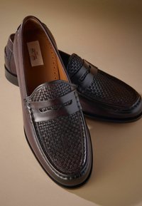 Braune Lederloafers mit gewobener Textur an der Vorderseite, flachen Sohlen und einer glatten Oberfläche. Enthält einen dekorativen Riemen über dem Blatt.