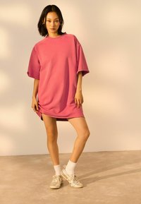Overgrote roze sweatshirt jurk met korte mouwen, ronde hals en zijsplitten. Gecombineerd met zilveren sneakers en witte crew-sokken.