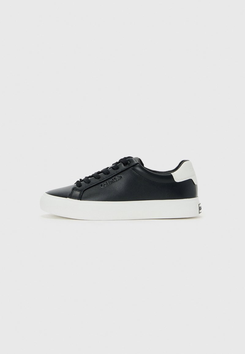 Baskets basses noires avec semelle blanche, lacets noirs, languette blanche au talon et nom de marque embossé sur le côté.