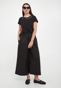 T-shirt nera a maniche corte con dettagli in bianco allo scollo, abbinata a pantaloni neri a gamba larga e scarpe basse in tessuto nere.