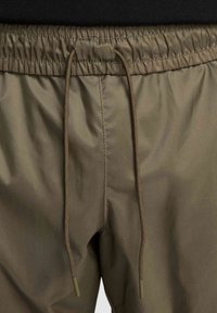 Olīvu zaļi šorti ar elastīgu jostasvietu, kam ir auklas aizdare un gluda, viegla auduma tekstūra.