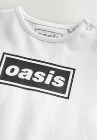 Weißes Baumwoll-T-Shirt mit einem schwarzen rechteckigen Grafikdesign, auf dem das Wort "oasis" in fetter, serifenloser Schrift erscheint. Mit Druckknopfdetail am Ausschnitt.