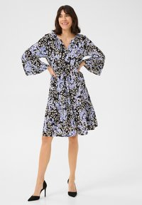 Schwarzes Kleid mit blauem und weißem Leopardenmuster. Mit einem V-Ausschnitt, lockeren Glockenärmeln und einer taillierten Taille. Glattes Stoffgefühl.