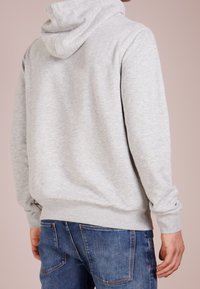 Sudadera de algodón gris con capucha ajustable, puños y cintura acanalados, combinada con jeans de mezclilla azules, mostrando un diseño liso en la parte posterior.