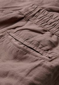 Tissu brun texturé avec un aspect froissé, comportant une taille élastique et une poche arrière avec un détail de bord cousu.