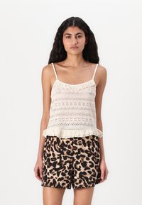 Camisole en dentelle crème avec un ourlet volanté, associé à un short léopard marron. La camisole présente des fines bretelles et une coupe ajustée.
