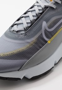 Grå idrottssko med ett meshuppdrag och reflekterande detaljer, texturerade overlay och en dämpad sula med en svart gummiyttersula.