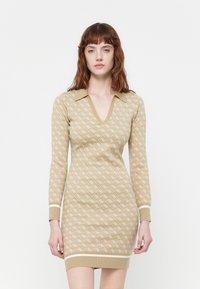 Rochie tricotată în bej cu un model alb în diamant, cu decolteu în V și guler. Mâneci lungi și tivuri ribbate completează designul.