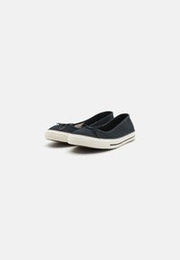 Mørkeblå kanvas slip-on sko med teksturert overflate, hvit gummisåle og liten sløyfedetalj foran. Holdbart og lett design.
