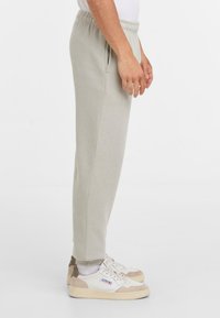 Zijaanzicht van een persoon die lichtgrijze sweatpants met elastische taille en witte sneakers met beige accenten draagt.